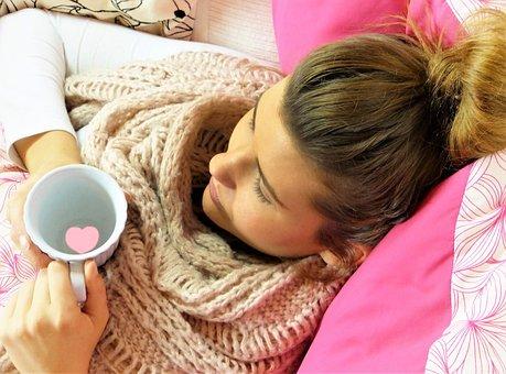 Nainen nojaa vaaleanpunaista tyynyä vasten ja juo teetä.